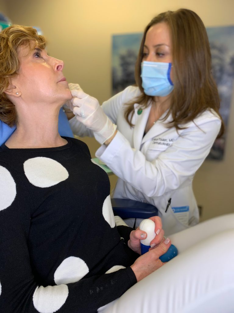 dr kristel polder from the dallas center for dermatology and aesthetics performing dermal fillers on a woman over 50 wearing black and white polka dot sweater