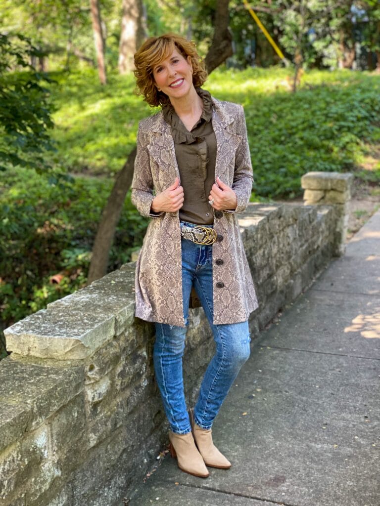 woman over 50 standing outside and wearing cabi icon blouse, cinch skinny, serpent belt, and king cobra jacket with vince camuto taupe suede booties