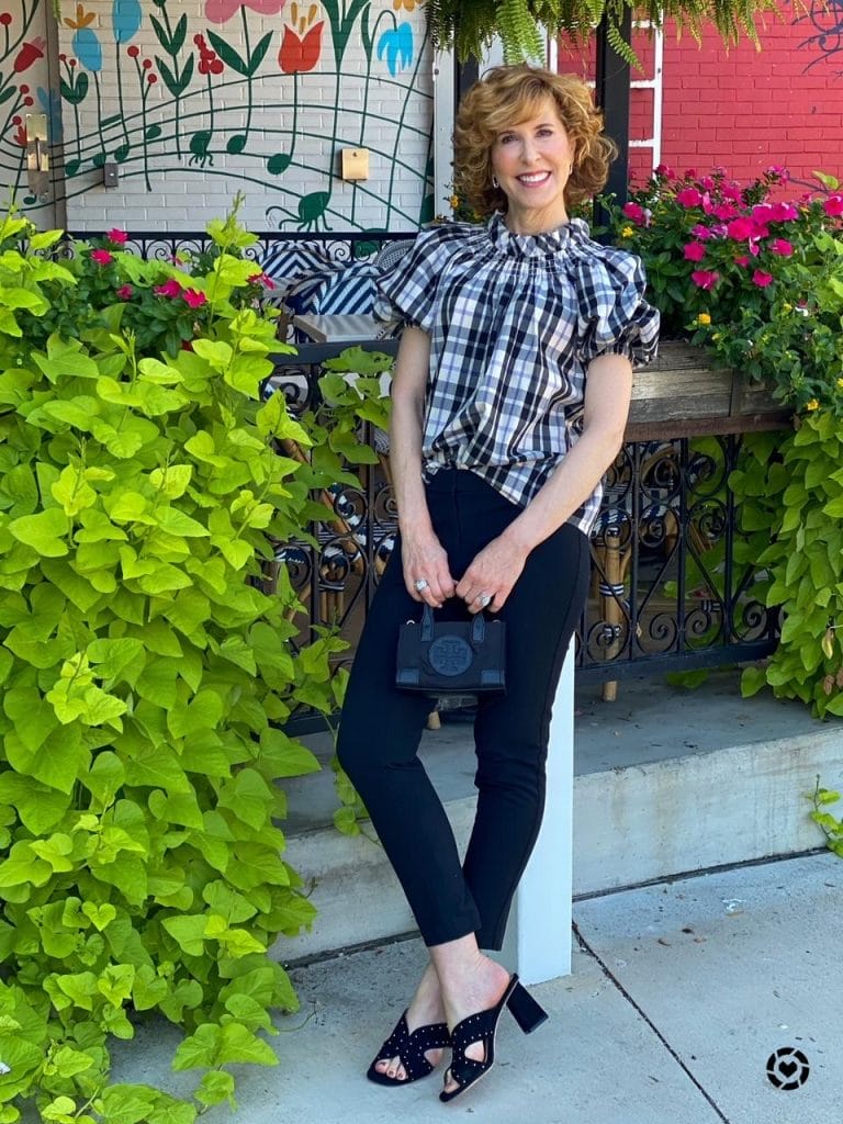 woman wearing jcrew plaid puff sleeve blouse and black pants leaning back against a pole carrying a tory burch micro bag