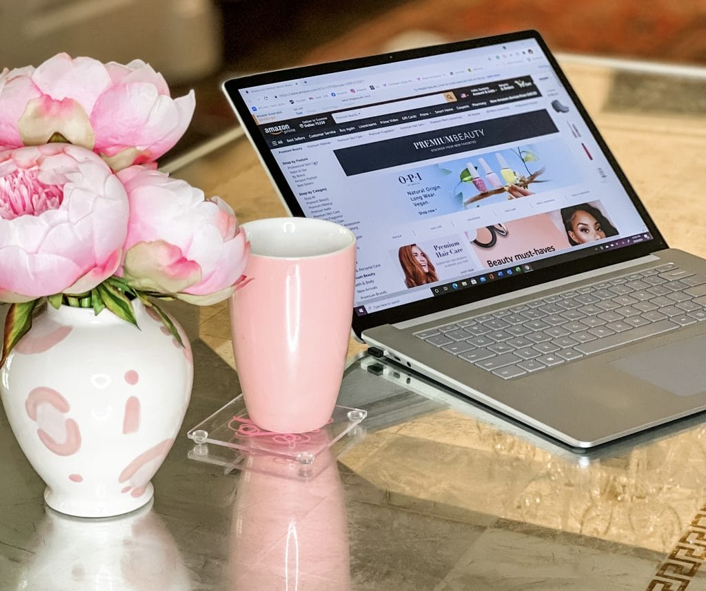 computer with screen on Amazon beauty page sittiing on a desk with pink flowers, vase, and pink mug