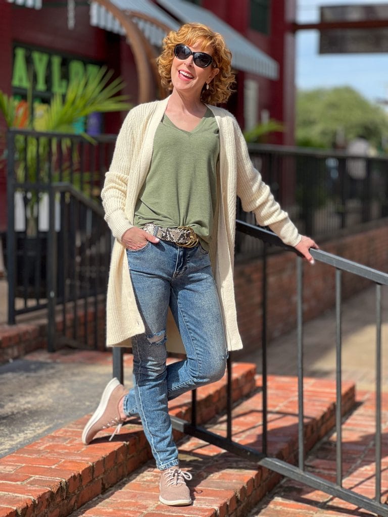 woman over 50 wearing cabi recline tee, cinch skinny jeans and book club cardigan standing on a brick staircase by a black railing