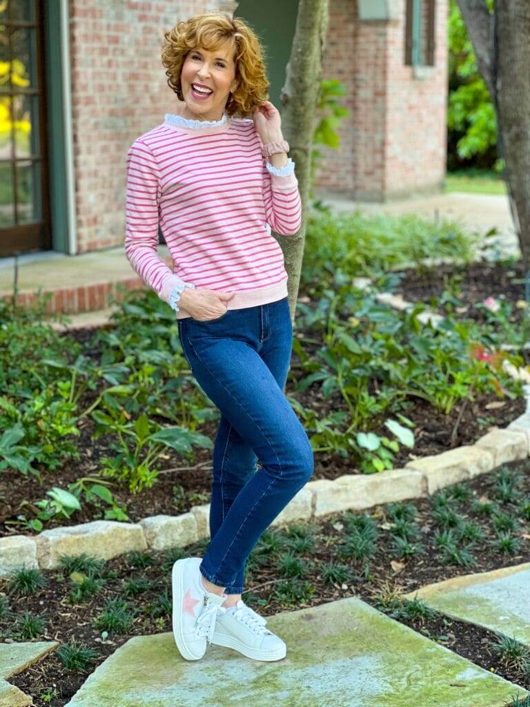 woman wearing boden pink striped sweatshirt with eyelet neck ruffle, jeans, and sole bliss pink star sneakers