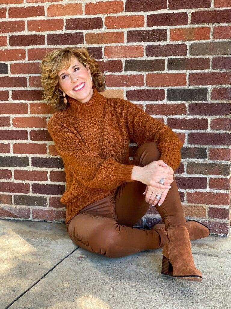 woman wearing brown turtleneck sweater and pants sitting on the ground by a brick wall