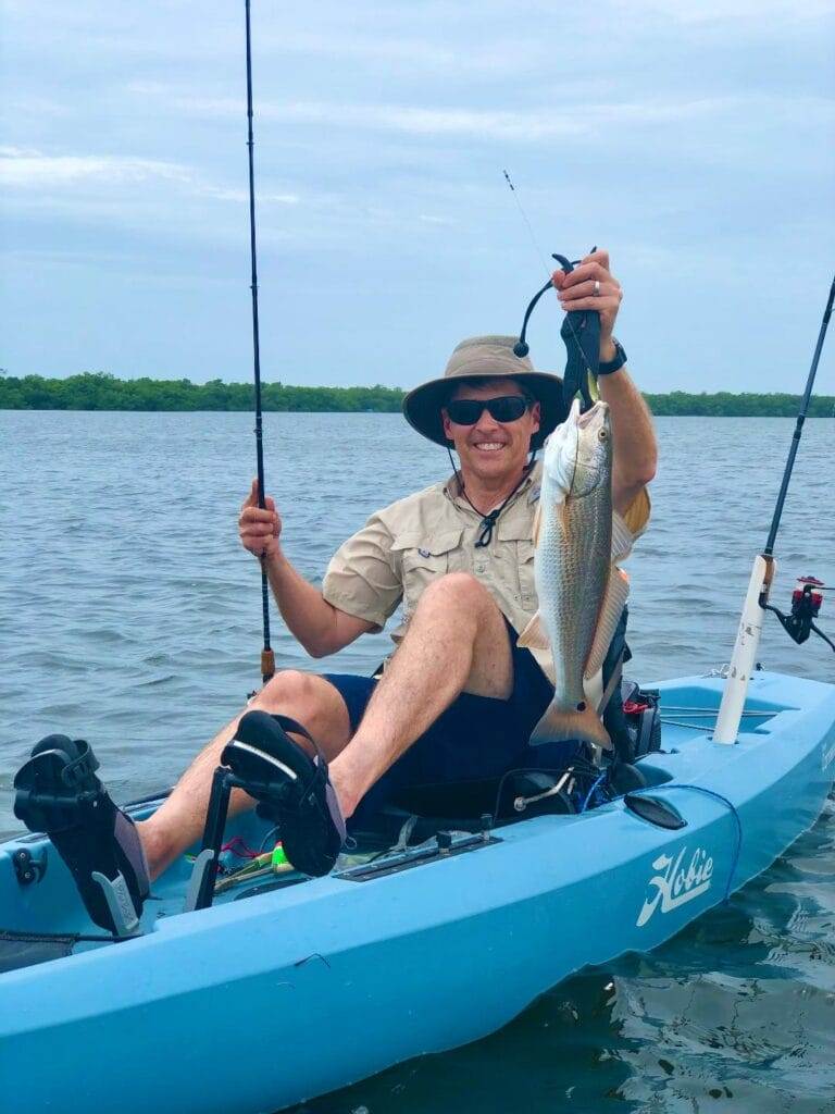 man holding up a fish from a blue Hobie kayak in tarpon bay on sanibel island