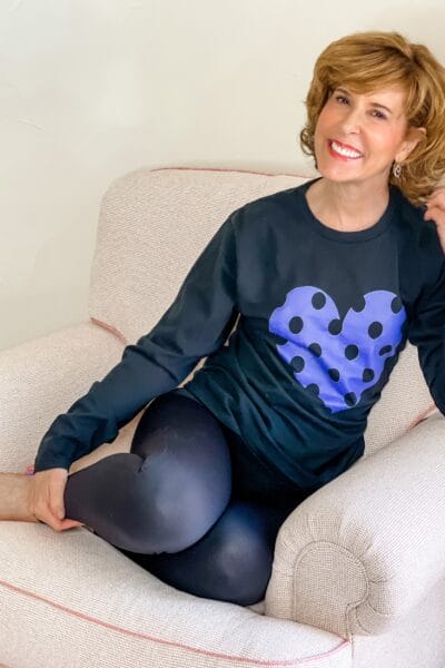 woman sitting in a chair wearing a black tee with a polka dot heart in very peri the pantone color of the year