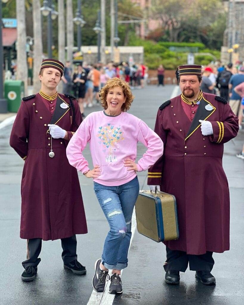 woman standing in front of the tower of terror hotel in disney's hollywood studios with hotel bellmen on either side