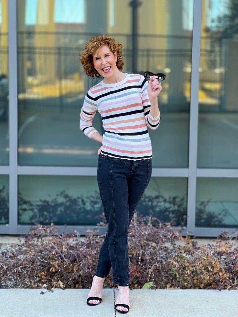 woman over 50 standing in front of a mirrored window wearing Halogen® Ribbed Crewneck Sweater and black seamed Mom jeans by Nordstrom showing how to transition your wardrobe from winter to spring with Nordstrom made brands