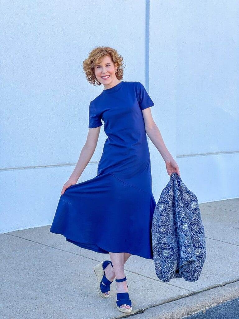 woman over 50 standing against white wall wearing Caslon® A-Line T-Shirt Cotton Maxi Dress from Nordstrom with navy wedges and holding a navy quilted patterned jacket