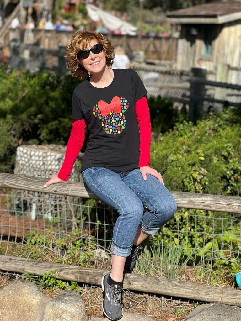 woman wearing black disney tee with polka dot minnie mouse with red bow sitting on a fence in frontierland at disney's magic Kingdom