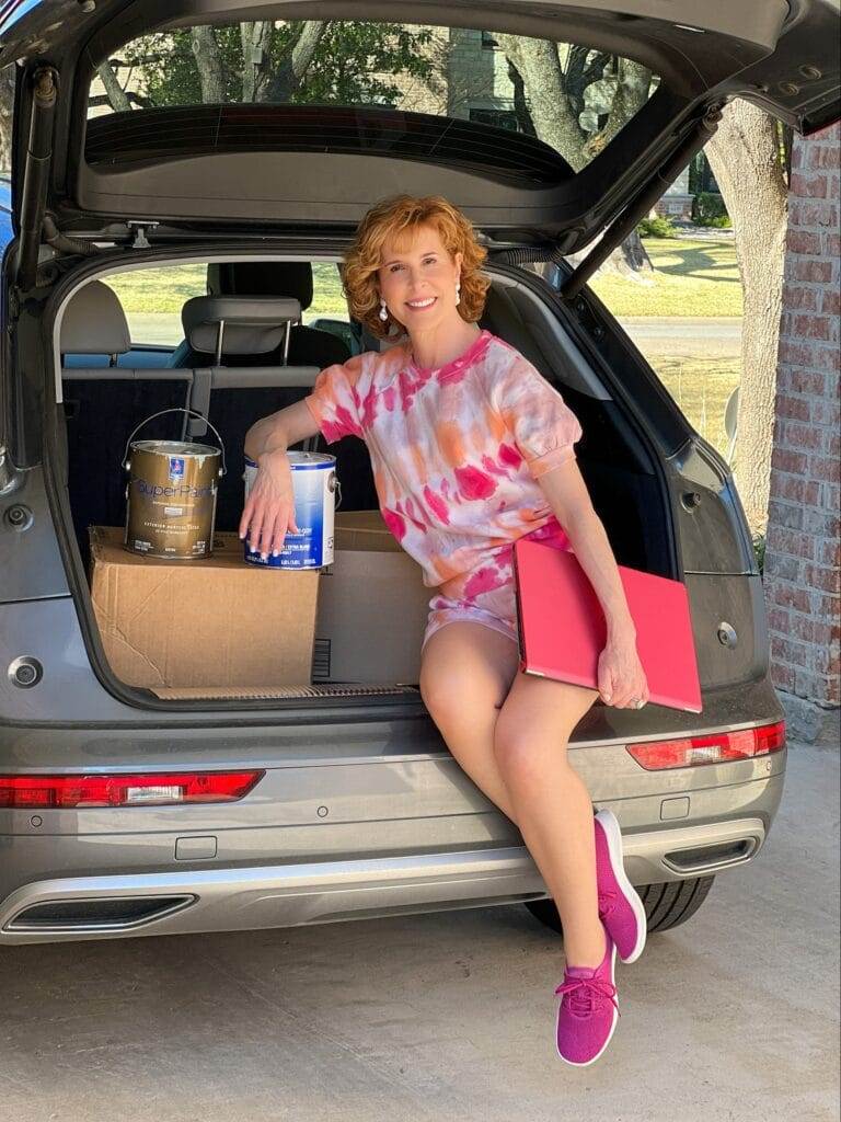 woman wearing tie dye shorts outfit sitting in the back of a car figuring out how to dispose of old laptop