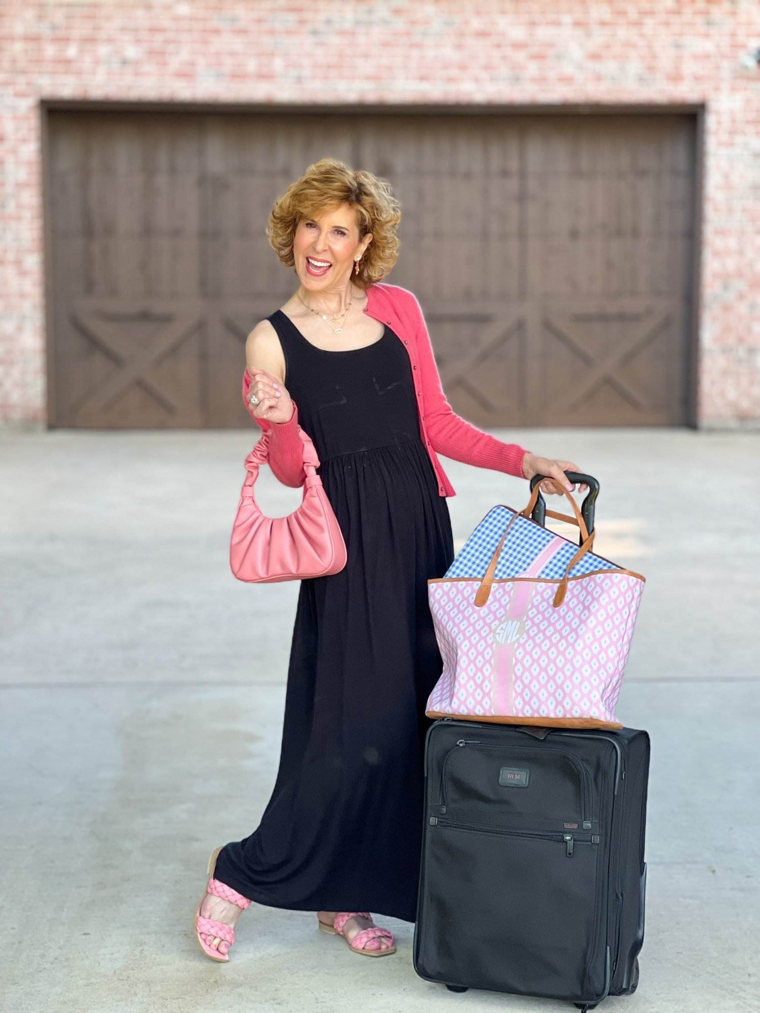 woman wearing Amazon black maxi dress and coral sweater standing next to luggage in driveway