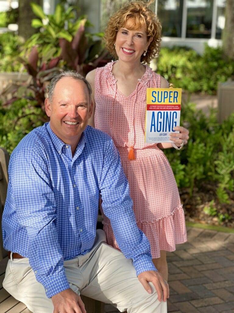 woman over 50 holding up book super aging with author sitting next to her