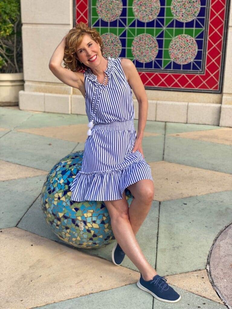 woman posing near a colorful wall wearing Navy Stripe Sleeveless Ruffle Dress sun protective clothing from cabana life