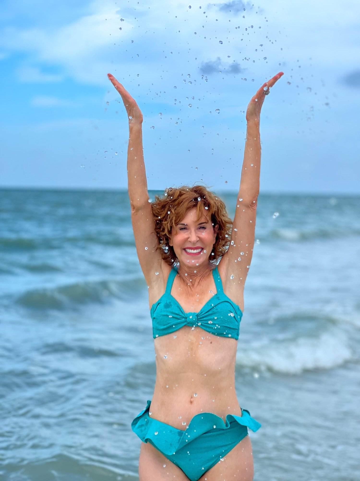 woman over 50 in blue bikini splashing in the water at the beach on sanibel island