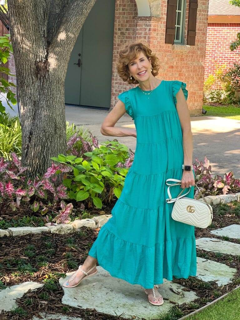 over 50 woman wearing teal lara dress from avara and white purse standing in front yard