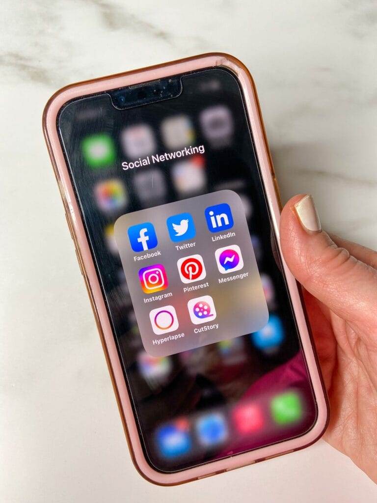 woman holding a phone showing social media apps on an iphone with a white marble background