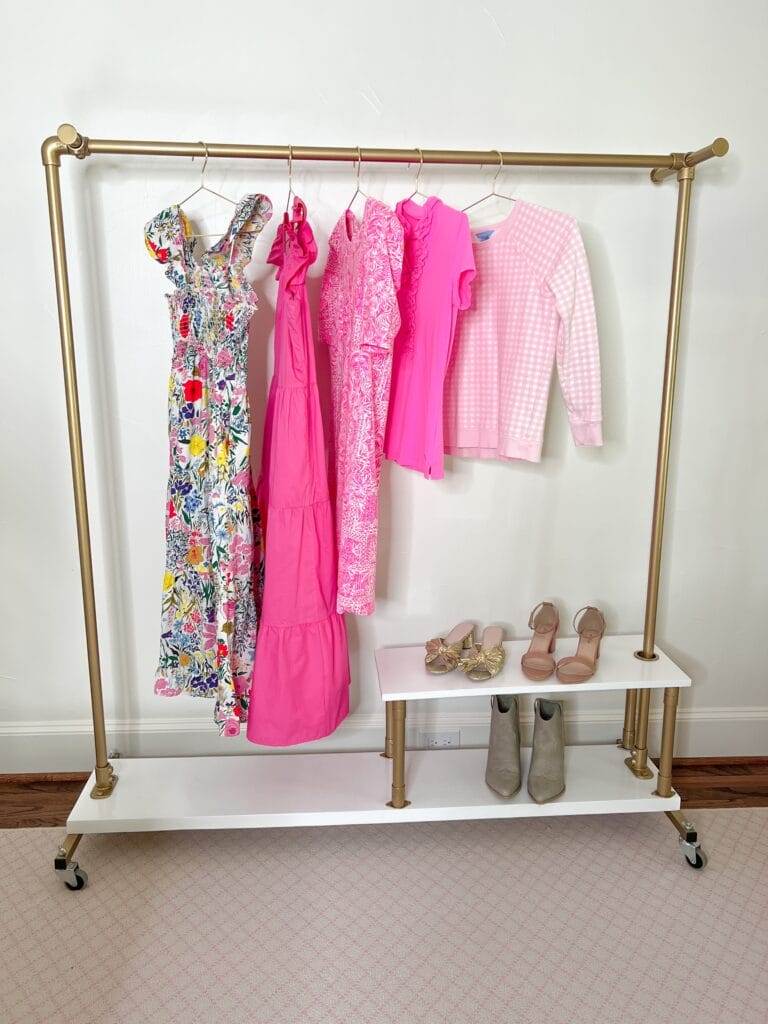 gold and white wheeled clothing rack with pink toned clothing hanging on it