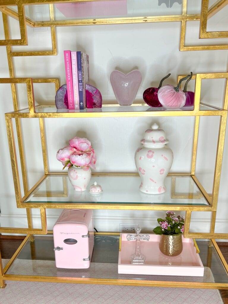 bottom three glass and brass shelving unit with pink toned accessories sitting on it