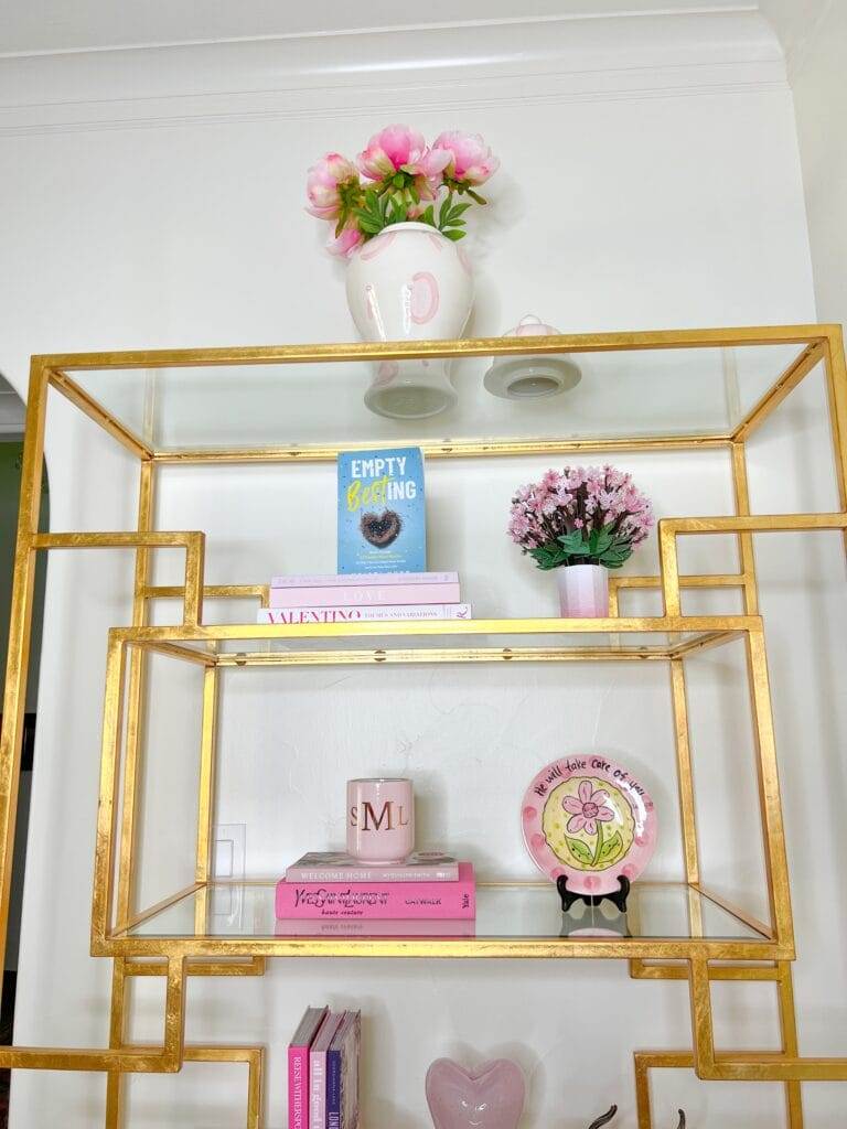 top shelves of glass shelving unit with pink toned accessories sitting on them