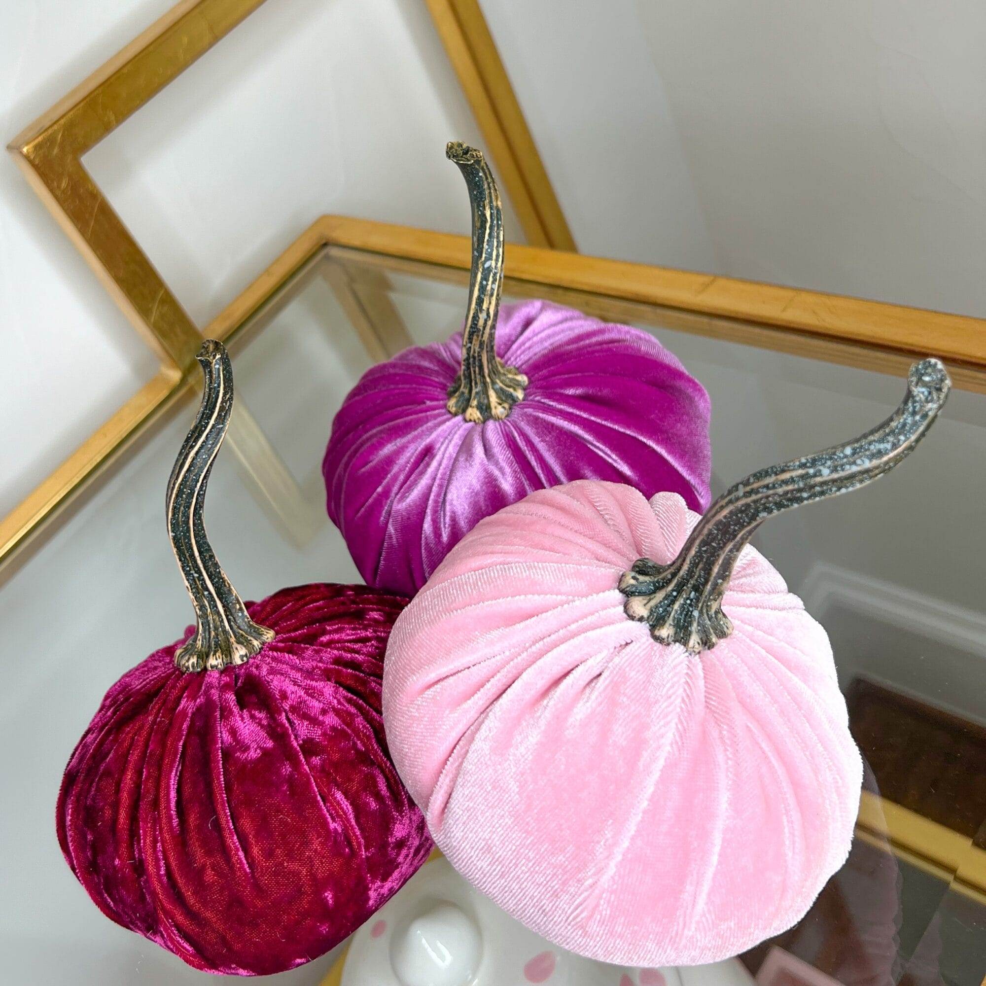 three pink velvet pumpkins sitting on a glass shelf