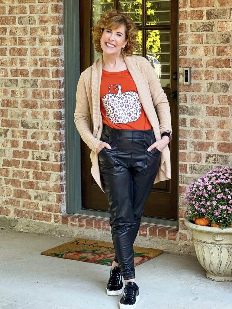 woman standing by her back door wearing a pumpkin tee and spanx faux leather joggers and barefoot dreams cardigan