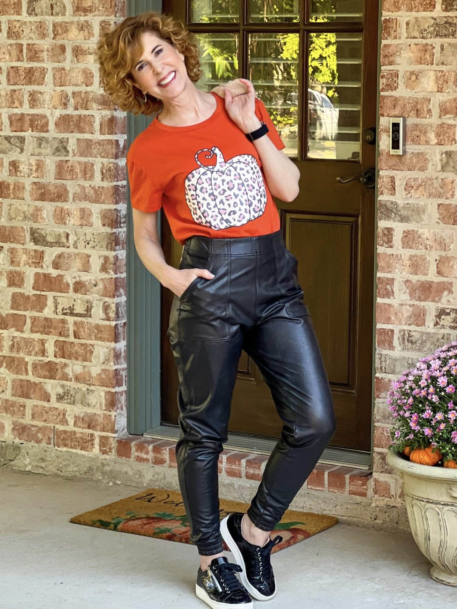 woman standing by her back door wearing a pumpkin tee and spanx faux leather joggers