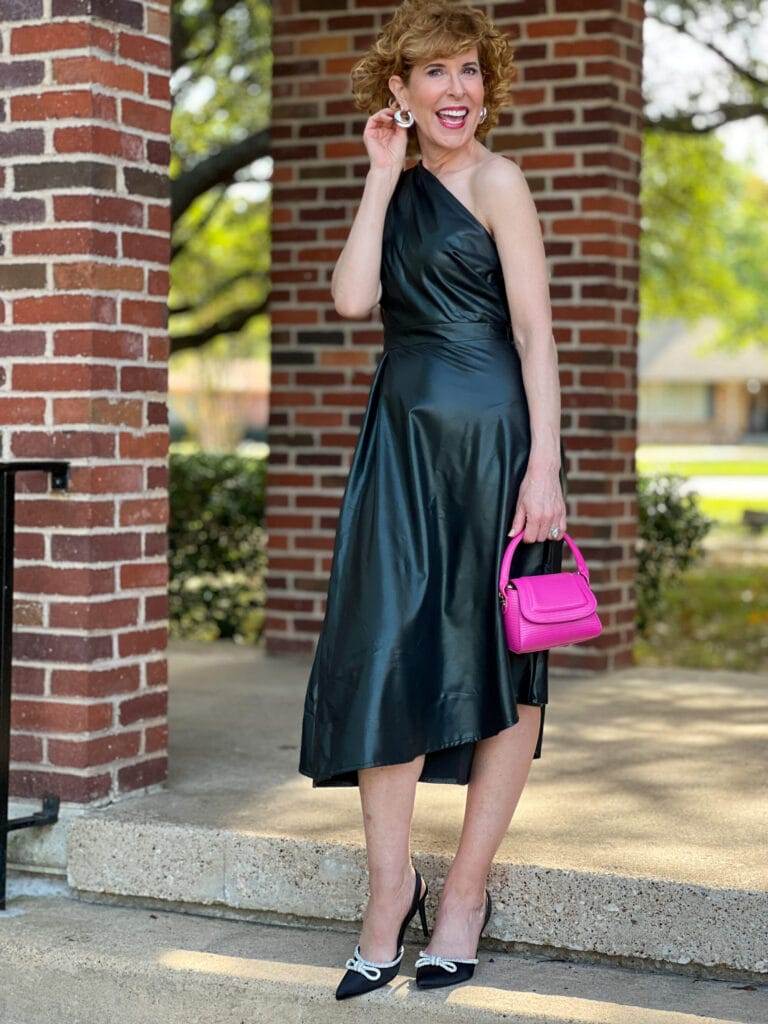 Woman over 50 standing on outside steps wearing Sofia Jeans by Sofia Vergara Women's One Shoulder Faux Leather Dress, Scoop Women's Embellished Sateen Slingback Pumps carrying Scoop Women's Mini Structured Bag all from Walmart