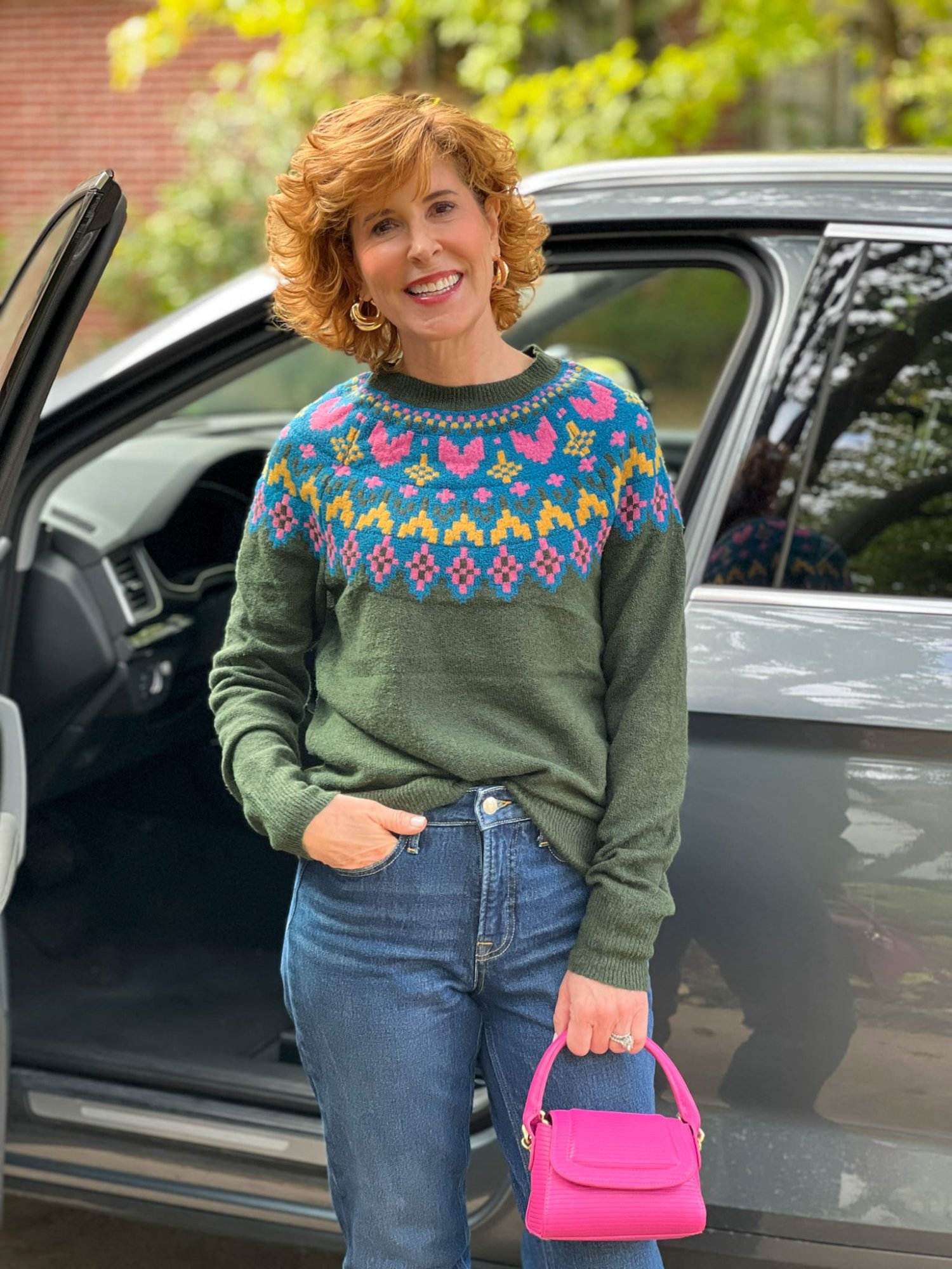 woman over 50 standing by a car wearing Walmart’s Time and Tru Women's Intarsia Sweater in green with pink hearts high waist jeans and carrying a pink mini handbagby a car wearing