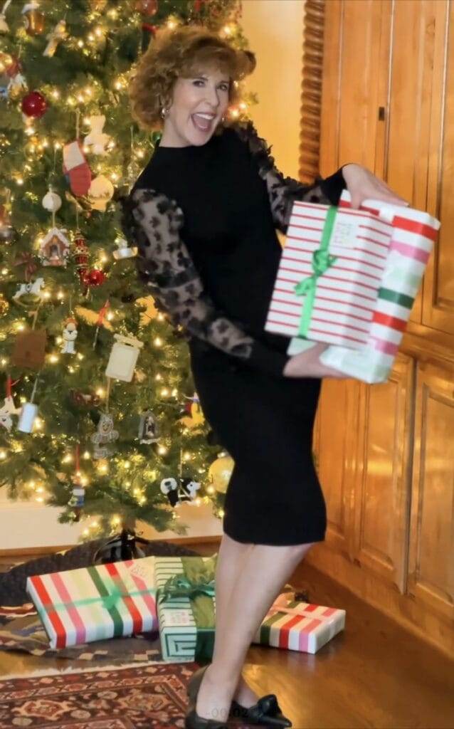 woman over 50 wearing black dress standing in front of the christmas tree holding two wrapped gifts