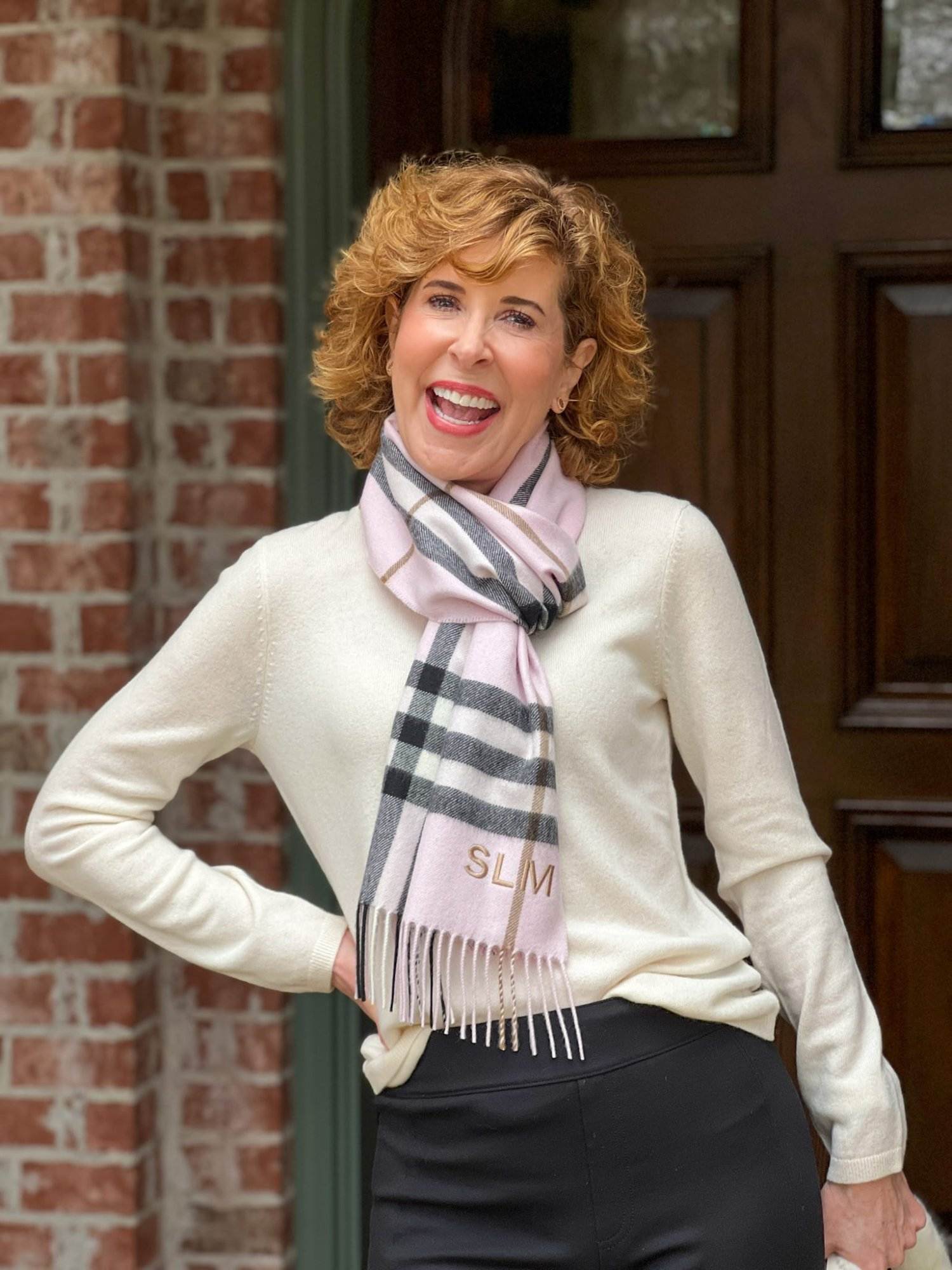 woman over 50 standing on front porch wearing ivory cashmere sweater with burberry scarf looking into the camera