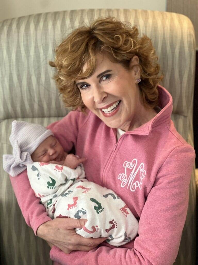 woman wearing pink monogrammed pullover holding a newborn baby