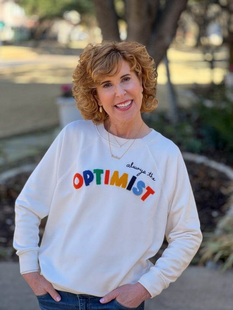 woman over 50 standing on driveway wearing loft's optimist sweatshirt