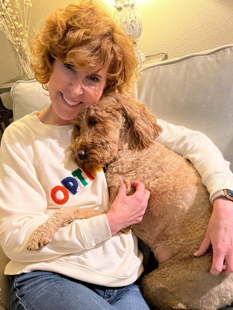 woman over 50 wearing loft's optimist sweatshirt and cuddling a goldendoodle