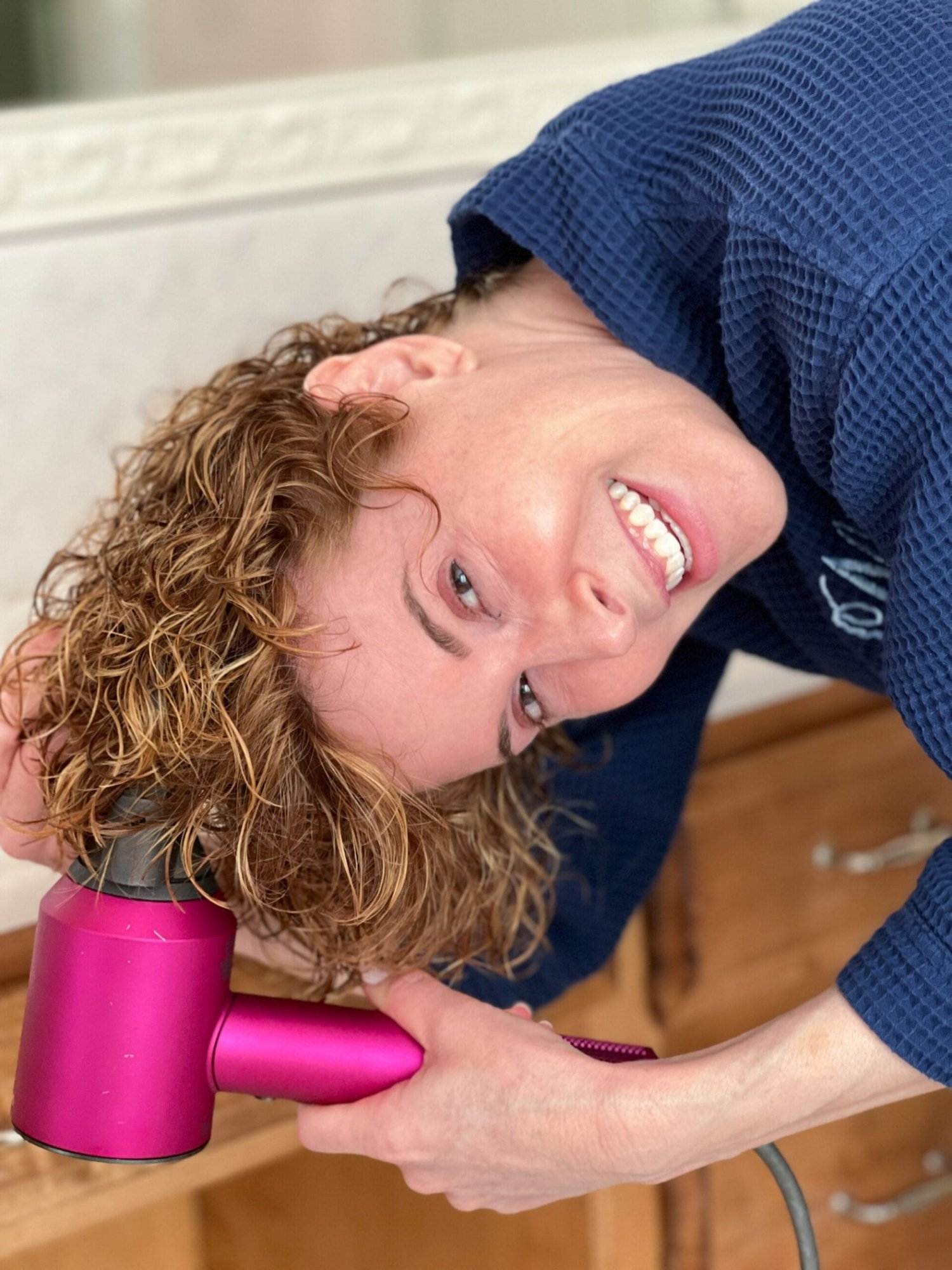 woman drying her aging hair upside down with hot pink blowdryer