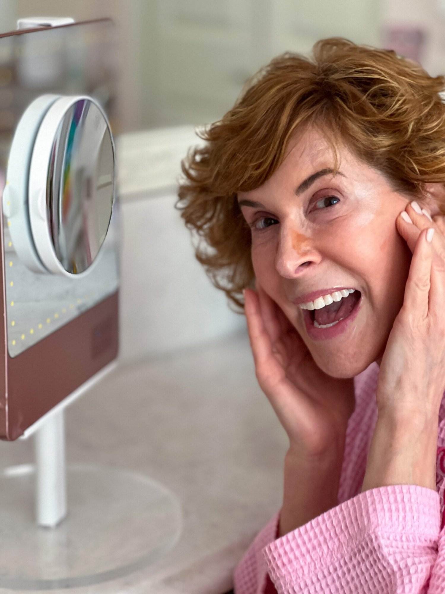 woman over 50 in front of a makeup mirror looking at the camera as she blends contour into her face