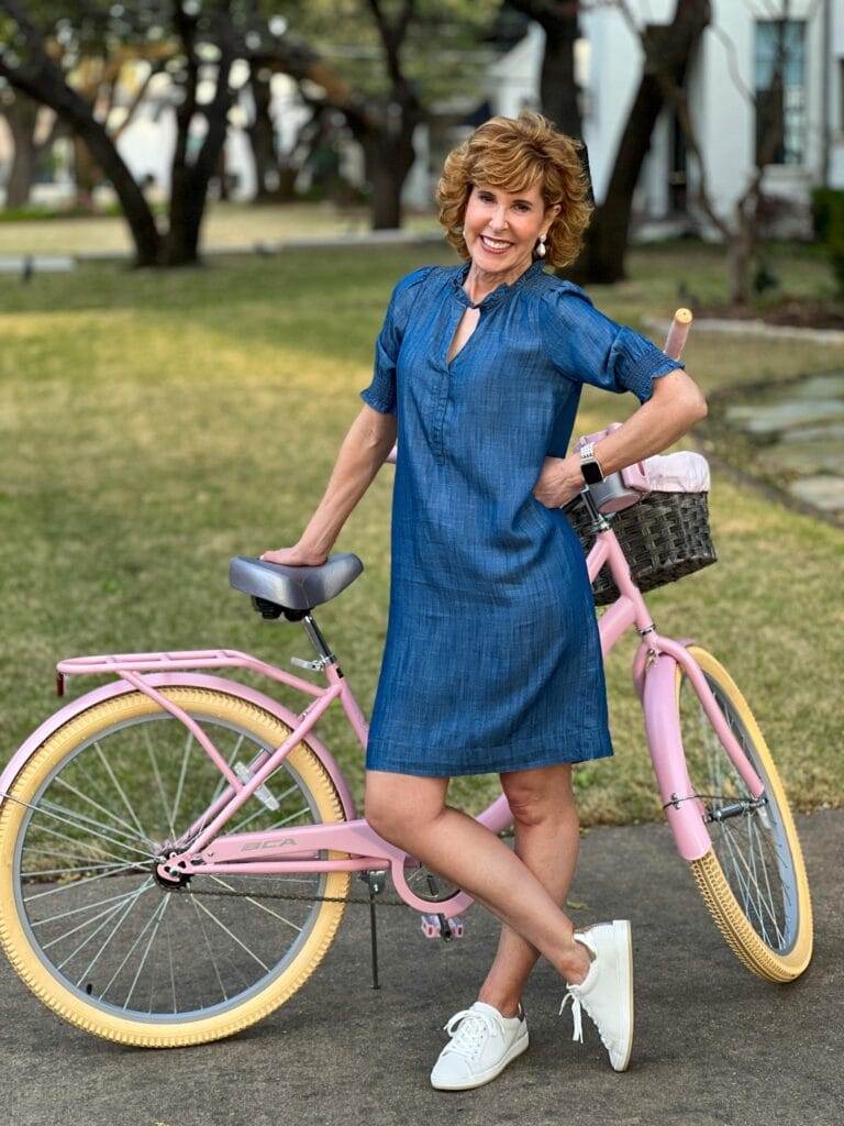 woman wearing denim shift dress standing next to a pink bike