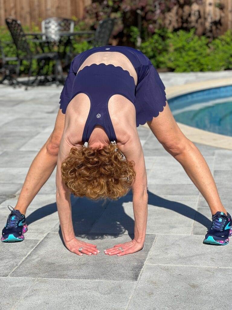 woman over 50 wearing navy blue scalloped workout set standing by a pool demonstrating a stretch