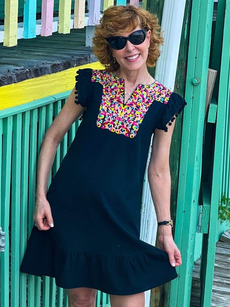 woman wearing black amazon dress with pom pom sleeves and colorful neckline against a colorful fence