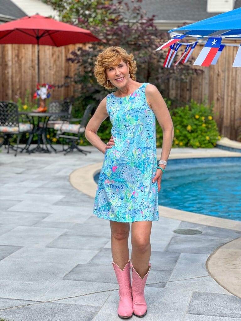 woman wearing lilly pulitzer texas dress and pink cowboy boots standing by a swimming pool