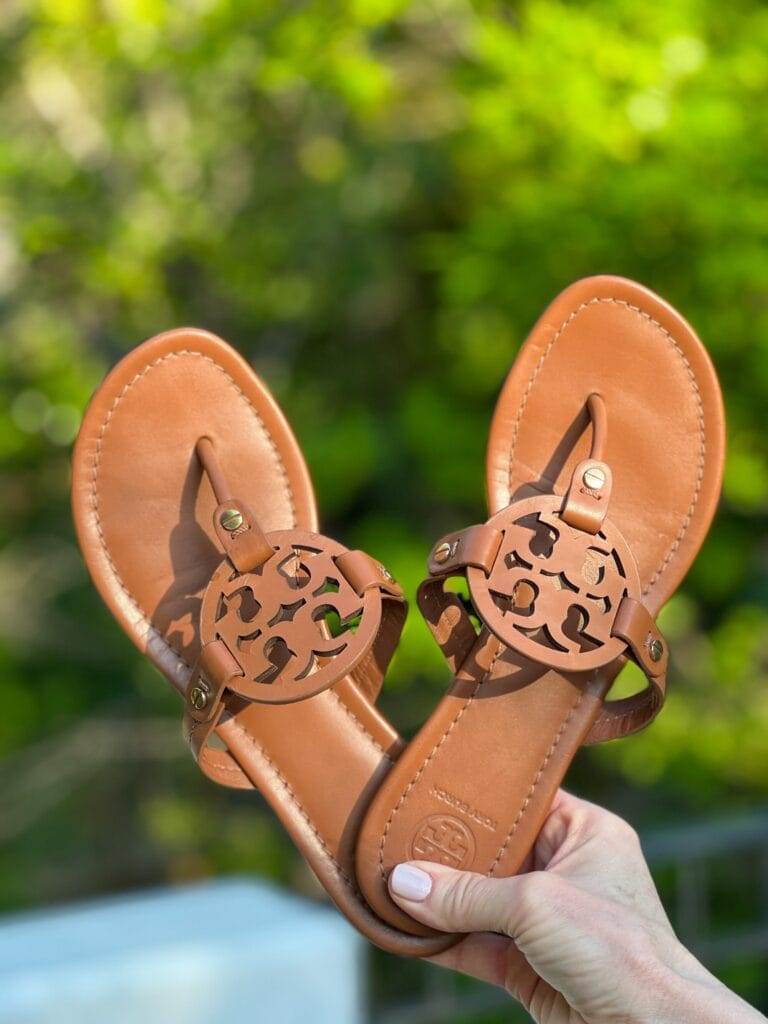 woman's hand holding tory burch miller flip flops in vintage vachetta
