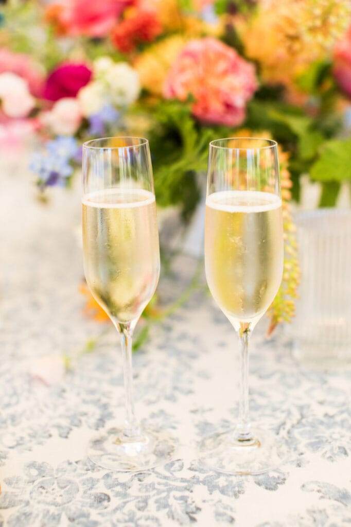 two champagne glasses and flowers behind