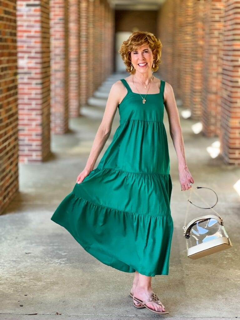 woman standing in green sleeveless dress holding clear stadium purse