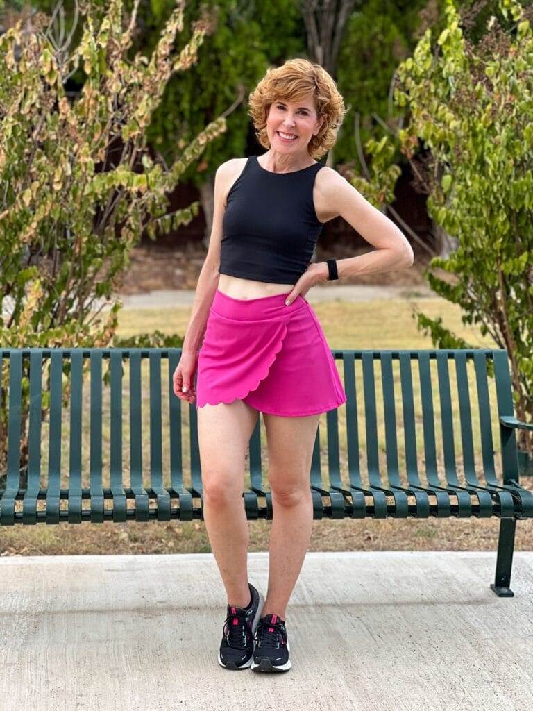 woman over 50 wearing black workout tank and hot pink scallop edge skirt workout wear