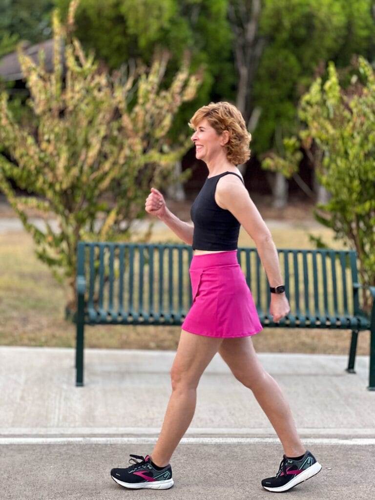 woman over 50 walking and wearing black workout tank and hot pink scallop edge skirt workout wear from shop the mint