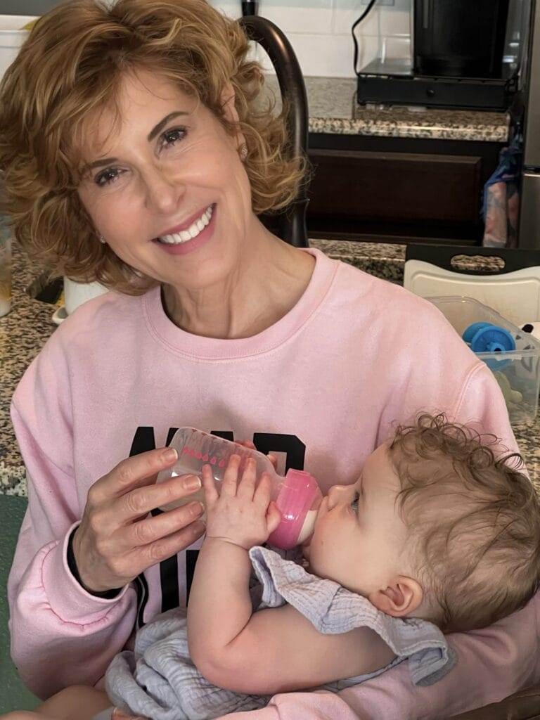 woman in pink sweatshirt giving a baby a bottle