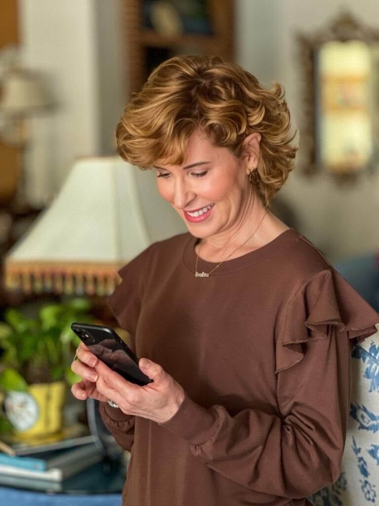 woman standing in living room looking at her iphone