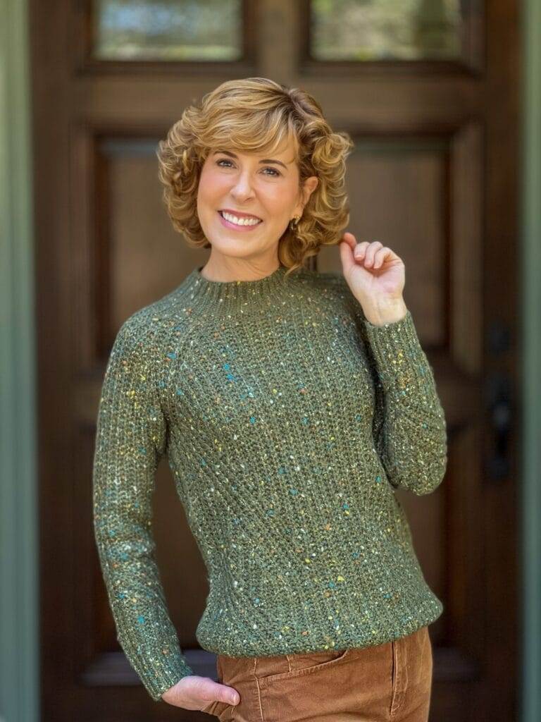 woman wearing green chunky tweed sweater standing by a door