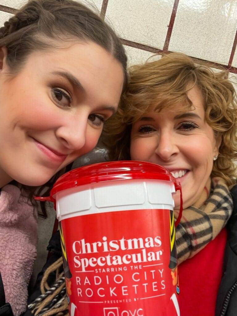 two women holding a bucket of popcorn from radio city christmas spectacular in nyc