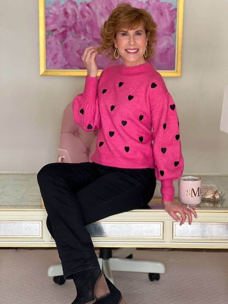 woman over 50 with legs crossed sitting on the edge of desk in office