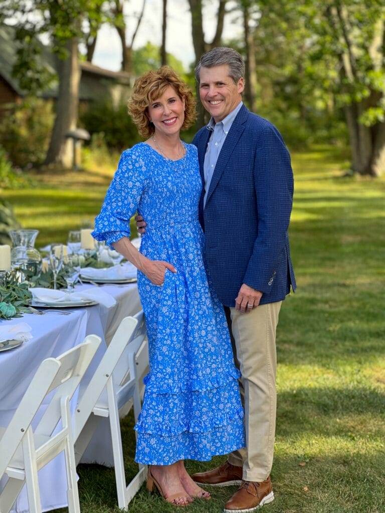 couple wearing blue outfits standing in a garden next to a white table